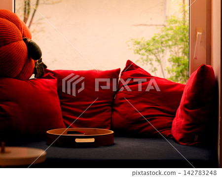Cozy window seat with plush red pillows and a decorative pumpkin Cozy window seat with plush red pillows and a decorative pumpkin 142783248