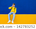 Young student talking on phone sitting on colorful wall 142783252