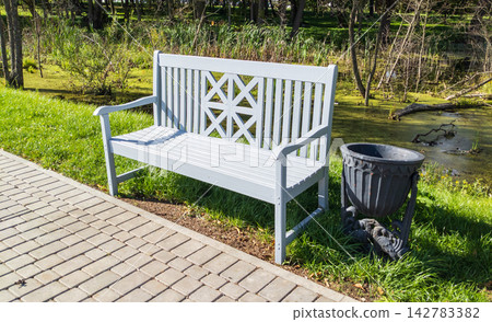 Wooden bench stand along a gravel path. Outdoor garden landscape with empty bench. 142783382