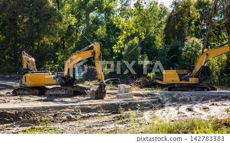 Yellow excavators excavating land for artificial lake. Heavy machinery prepares site Yellow excavators excavating land for artificial lake. Heavy machinery prepares site 142783383