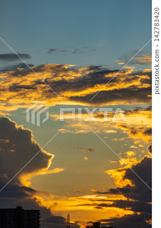 Dramatic sunset clouds illuminated by golden light over city skyline Dramatic sunset clouds illuminated by golden light over city skyline 142783420