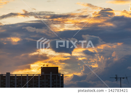 Dramatic sunset clouds illuminate apartment building rooftop with antennas 142783421