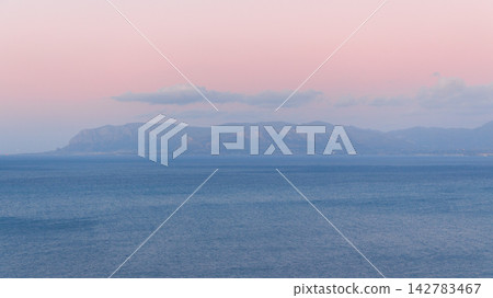 Serene pastel sky over calm blue sea and distant hazy mountains at horizon Serene pastel sky over calm blue sea and distant hazy mountains at horizon 142783467