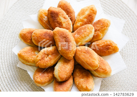 Freshly baked golden pirozhki pies placed on plate for bakery banner Freshly baked golden pirozhki pies placed on plate for bakery banner 142783629
