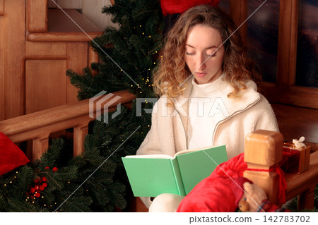 Young woman reading a book by a decorated Christmas tree on Christmas Eve Young woman reading a book by a decorated Christmas tree on Christmas Eve 142783702