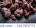 Close-up of chocolate coated nuts dusted with cocoa powder on a dark ceramic background.  142783772