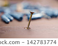 Golden metallic screw inserted crookedly into a wooden surface with blurred plastic wall plugs in the background. Construction mistake and home renovation failure concept 142783774