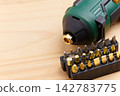 Modern green cordless electric screwdriver on wooden table. Black plastic holders filled with various golden and gray precision bits 142783775