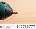 Screwdriver bit mounted in a cordless power drill on brown background. 142783777