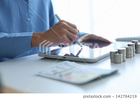 Close-up hand using digital tablet for tracking or analyzing financial data for budgeting and planning. Close-up hand using digital tablet for tracking or analyzing financial data for budgeting and planning. 142784219