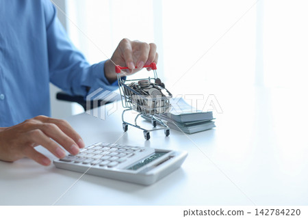 Miniature shopping cart filled with coins and stack of money on white table. Financial planning and E-commerce concept. 142784220