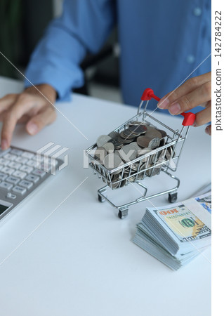Miniature shopping cart filled with coins and stack of money on white table. Financial planning and E-commerce concept. 142784222