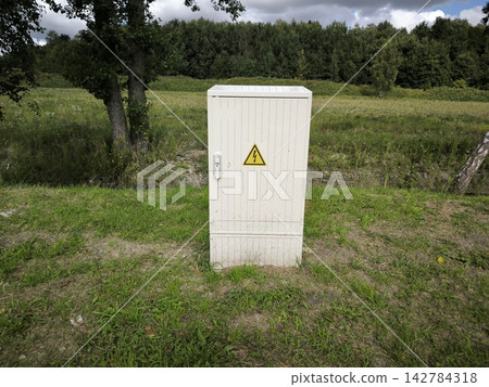 White electrical cabinet in the middle of a green field near the forest White electrical cabinet in the middle of a green field near the forest 142784318