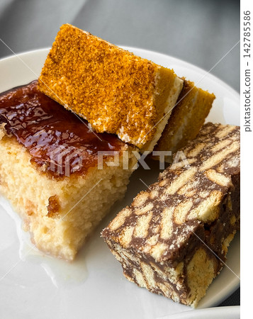 Three types of different shape and color desserts on white plate. One piece with glossy surface, other with layered design. Tasty sweets, fresh food product Three types of different shape and color desserts on white plate. One piece with glossy surface, other with layered design. Tasty sweets, fresh food product 142785586