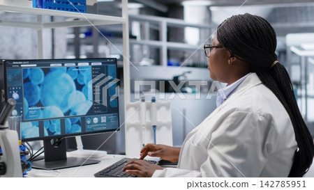 African American woman researcher examining compound in flasks and containers during laboratory testing, studying molecular content with biotechnology equipment. Genetics research. African American woman researcher examining compound in flasks and containers during laboratory testing, studying molecular content with biotechnology equipment. Genetics research. 142785951