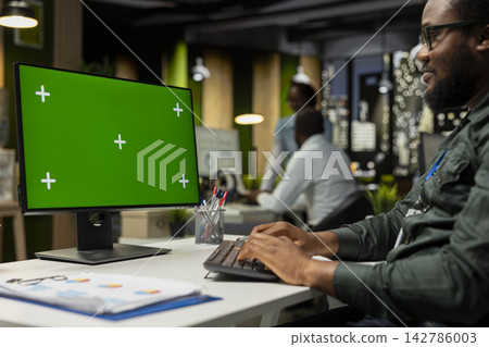 Mockup screen on desktop pc next to young black businessman reviewing data, working on analytics report writing and finding solutions for global expansion and business management tasks. Mockup screen on desktop pc next to young black businessman reviewing data, working on analytics report writing and finding solutions for global expansion and business management tasks. 142786003
