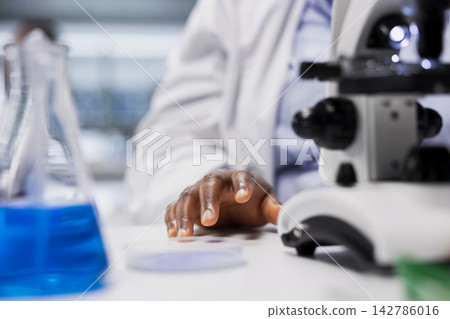 Close up of cytotechnologist inspecting new drug compound under microscope lens. Quality control analyst verifying medication quality and purity standards with optical device 142786016