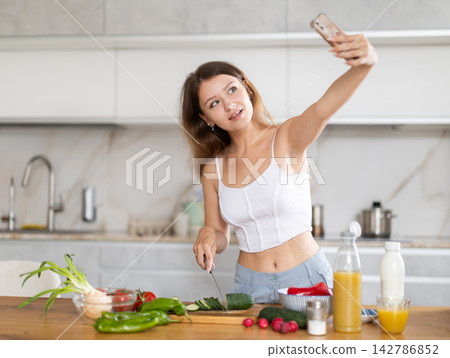 Pretty young girl in home T-shirt and shorts cooking salad and shoots content for social networks using smartphone on kitchen Pretty young girl in home T-shirt and shorts cooking salad and shoots content for social networks using smartphone on kitchen 142786852