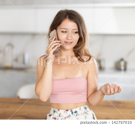 Young woman talking on mobile phone in kitchen Young woman talking on mobile phone in kitchen 142787010