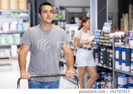 Positive man shopping in construction materials store, pushing cart 142787015