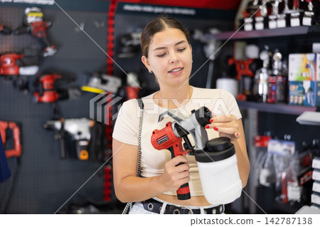 Woman chooses and buys paint spray gun in hardware store Woman chooses and buys paint spray gun in hardware store 142787138