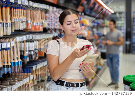 Woman examines product in paint shop and scans QR code on label of brush for painting concrete walls Woman examines product in paint shop and scans QR code on label of brush for painting concrete walls 142787139