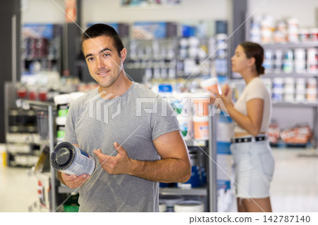 Man buys tin with paint in paintwork material store for carrying out internal finishing work on object 142787140