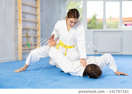 Woman and man practice grabbing and throwing on sports mats during judo training in gym Woman and man practice grabbing and throwing on sports mats during judo training in gym 142787161