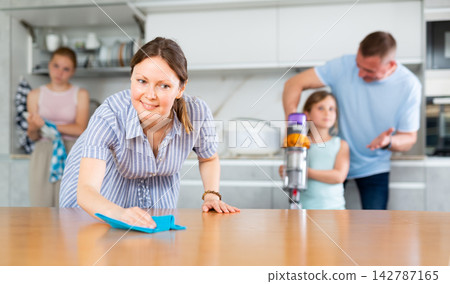 Woman rubbing table in kitchen while cleaning house with family Woman rubbing table in kitchen while cleaning house with family 142787165