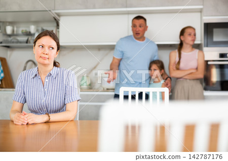 Offended wife sits at table and listens as her husband yells at her Offended wife sits at table and listens as her husband yells at her 142787176