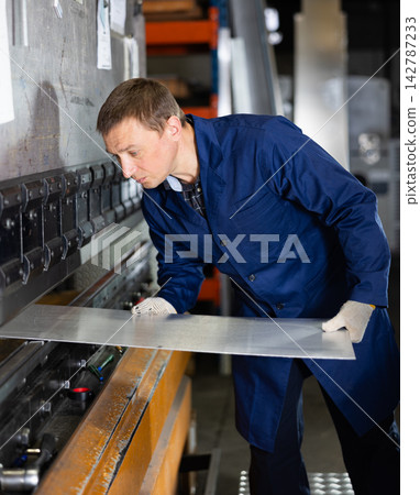 Craftsman positioning metal workpiece on bending machine in workshop Craftsman positioning metal workpiece on bending machine in workshop 142787233