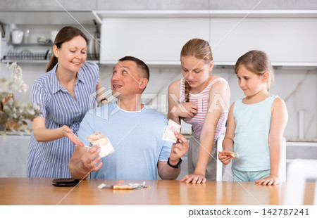 Father gives pocket money to children and wife in kitchen Father gives pocket money to children and wife in kitchen 142787241