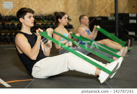 Young man exercising with resistance band loop during group training Young man exercising with resistance band loop during group training 142787281