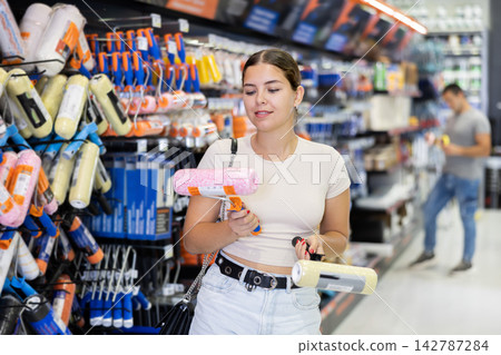 Interested young girl looking for rollers in painting supplies store 142787284