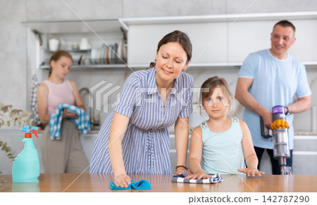 Friendly family tidy up room together. Mom and daughter are dusting the table. Father and daughter vacuuming room 142787290
