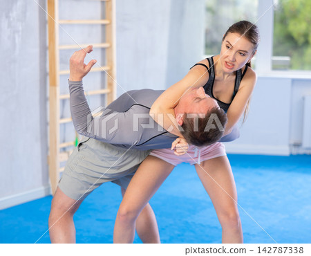 Young woman learning to do power grab on an opponent neck during self-defense training at gym Young woman learning to do power grab on an opponent neck during self-defense training at gym 142787338
