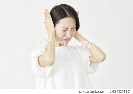Middle-aged woman covering her ears against a white background. Middle-aged woman covering her ears against a white background. 142787417