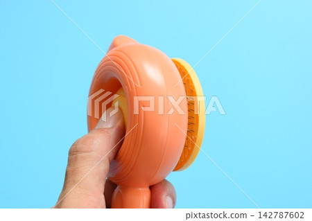 finger push on pastel orange comb on blue background, hair brush for pet 142787602