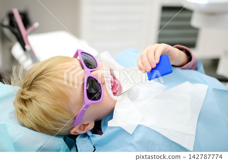 A young patient at a dental hygienist appointment in a modern medical center. A teenager is preparing for a professional teeth cleaning procedure. A young patient at a dental hygienist appointment in a modern medical center. A teenager is preparing for a professional teeth cleaning procedure. 142787774