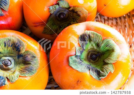 A simple scene with persimmons on a bamboo basket against a white background, representing the taste of autumn. A simple scene with persimmons on a bamboo basket against a white background, representing the taste of autumn. 142787938