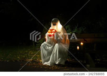 depicts a spooky ghost holding a glowing pumpkin on a dark night. A lit candle and bats set the scene for a festive Halloween celebration, decoration, and tradition. depicts a spooky ghost holding a glowing pumpkin on a dark night. A lit candle and bats set the scene for a festive Halloween celebration, decoration, and tradition. 142788093