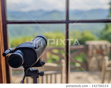 Spotting scope on tripod pointed out cabin window Spotting scope on tripod pointed out cabin window 142788314