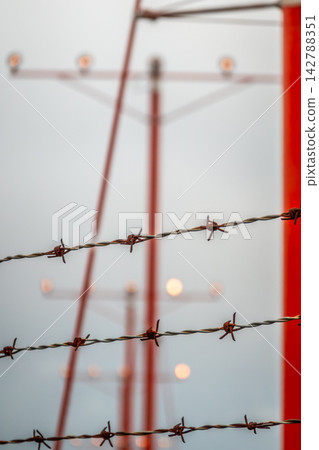 Commercial aircraft on final approach framed by security barbed wire fencing and bright red airport approach lighting systems Commercial aircraft on final approach framed by security barbed wire fencing and bright red airport approach lighting systems 142788351