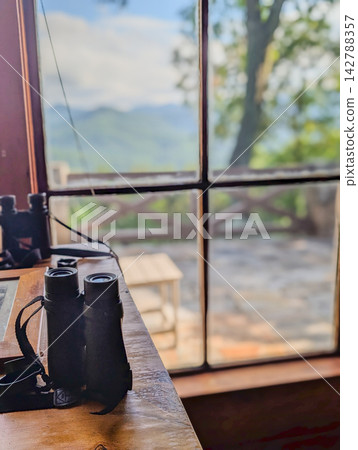 Binoculars on wooden desk by mountain view window Binoculars on wooden desk by mountain view window 142788357