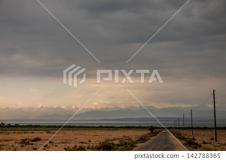Dirt road and utility poles leading toward Issyk Kul lake Kyrgyzstan Dirt road and utility poles leading toward Issyk Kul lake Kyrgyzstan 142788365