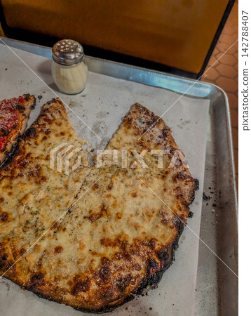 Thin crust pizza slices on baking tray with shaker Thin crust pizza slices on baking tray with shaker 142788407