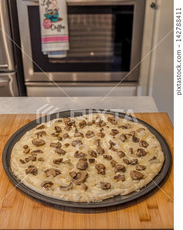 Unbaked pizza topped with cheese and mushrooms Unbaked pizza topped with cheese and mushrooms 142788411