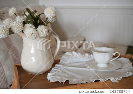 Elegant Teacup and Floral Arrangement on a Wooden Tray in a Cozy Bedroom Setting Elegant Teacup and Floral Arrangement on a Wooden Tray in a Cozy Bedroom Setting 142788734