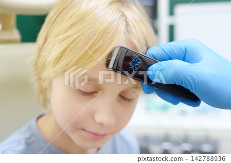 A pediatrician measures a young patient's temperature in the doctor's office. The electronic thermometer shows a temperature of 36.6 degrees. 142788936