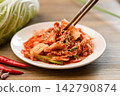 Eating kimchi cabbage on white plate with chopsticks, Korean homemade fermented side dish food 142790874